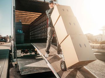 Mover walking down the ramp of moving truck with hand truck full of boxes
