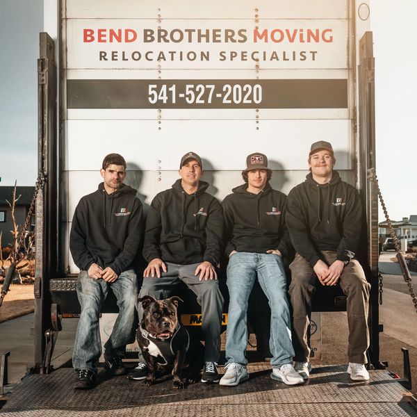 Bend Brothers Moving Employees sitting at the back of moving truck with adorable dog in front 
