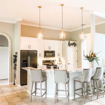 White kitchen with stainless steel appliances, three lamps, and four chairs around a kitchen counter