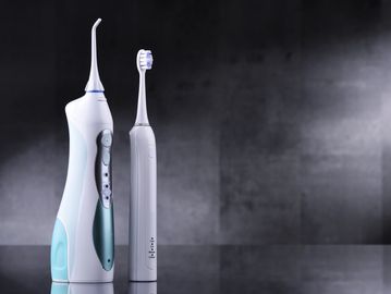 Water flosser stand next to electric toothbrush against a grey background