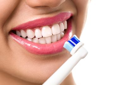 Electric toothbrush head by woman's mouth showing white clean teeth.