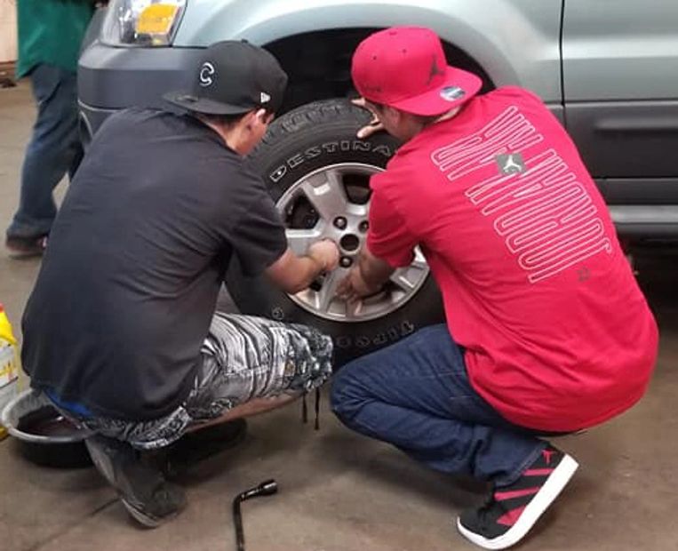 Young adults taking off a tire in the auto shop.