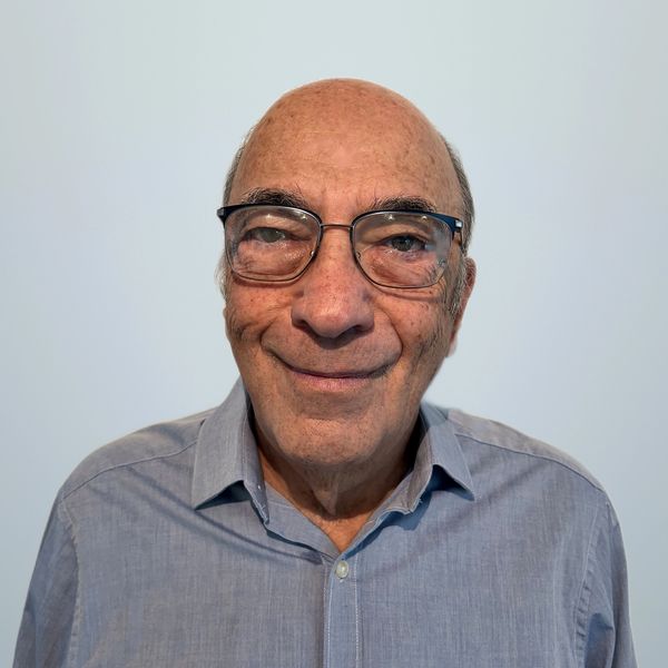 Smiling elderly man with glasses and blue shirt.
