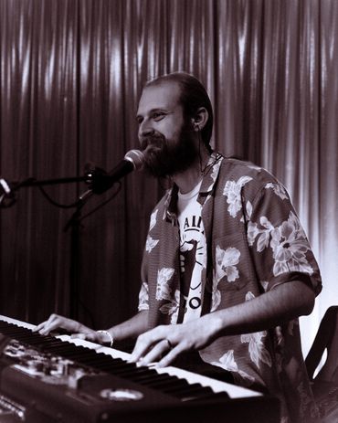 Man playing keyboard and singing into microphone with a smile.