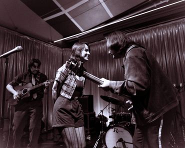 A band performs live with a female singer and guitarists on stage.