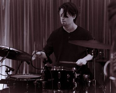 A drummer intensely playing a drum set on stage.
