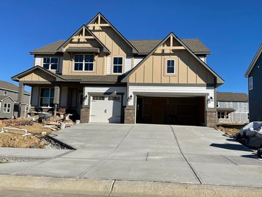 Newly constructed two-story house with fresh concrete driveway under a clear blue sky.