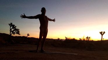 Silhouette of a person with arms outstretched at sunset in a desert landscape.
