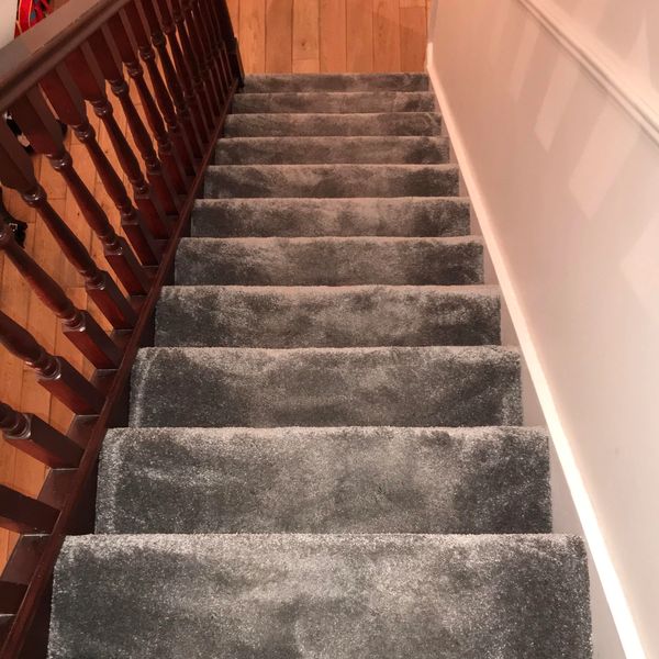 Carpeted stairs with wooden railing leading down to a wooden floor.