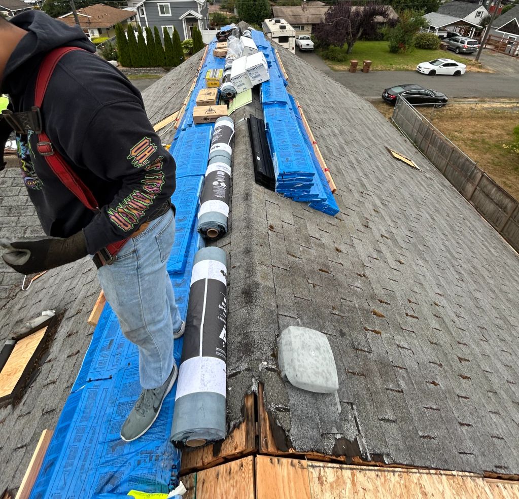 Roof repair in progress with materials and a worker on a damaged roof.