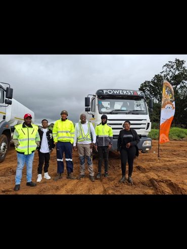 Six people standing in front of a Powerstar truck on a dirt road.