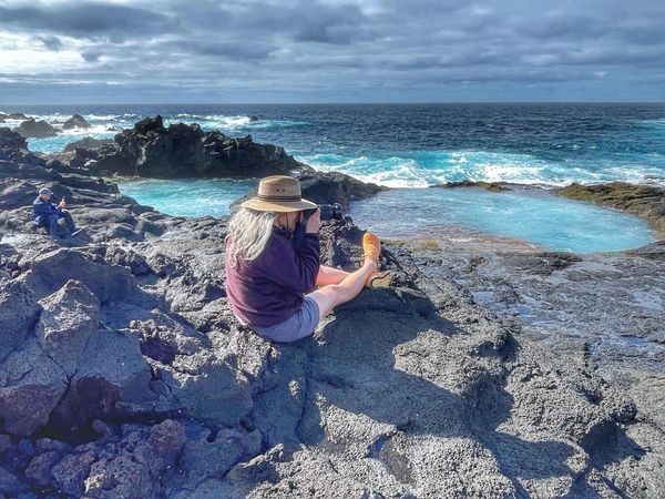 woman photographing the ocean on a rocky tidal pool on holiday in the Azores from Sao Miguel Island