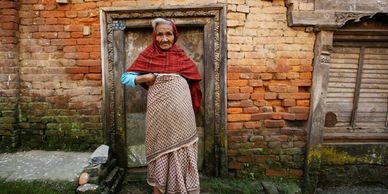 An elderly woman stands with her hand on her hip in front of her home in a remote village in Nepal