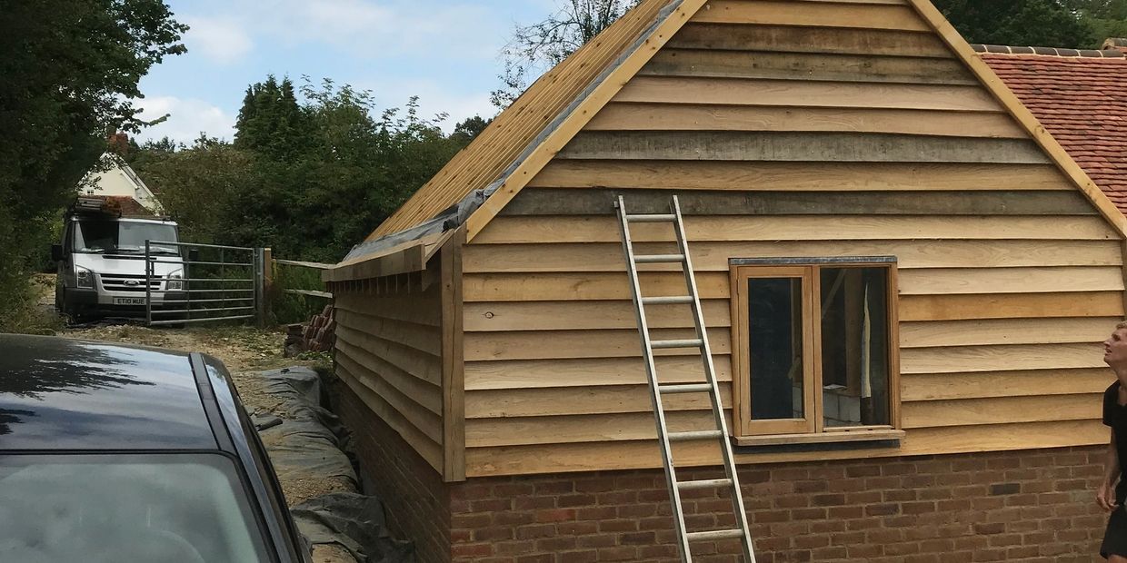 Wooden house under construction with ladders and vehicles nearby.