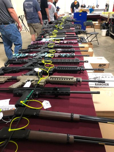 A display table with various rifles lined up for sale at an indoor event.