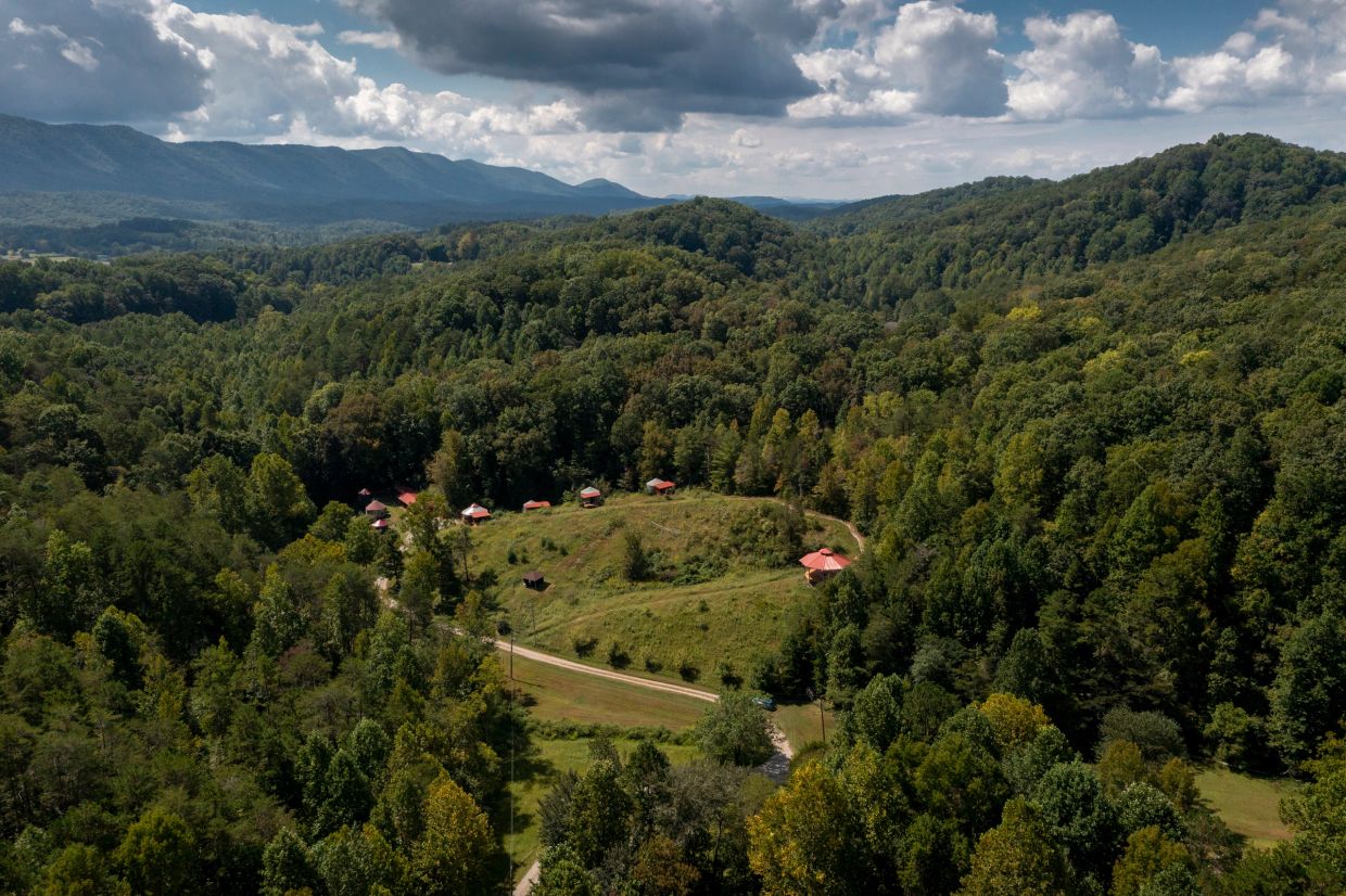 Aerial view of green forested hills and scattered red-roofed houses.