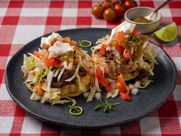 Two savory tostadas topped with lettuce, tomatoes, beans, and sour cream on a dark plate.