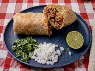A burrito cut in half with chopped onions, cilantro, and a lime wedge on a blue plate.