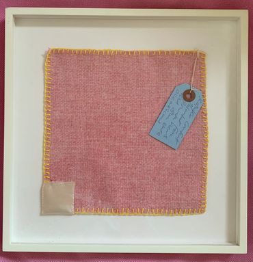 Framed pink wool fabric with yellow stitching and a blue tag.