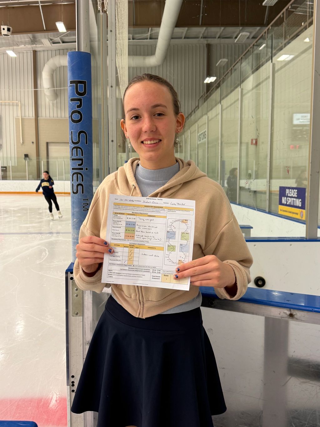 Young female figure skater proudly holding her test result sheet at an ice rink.