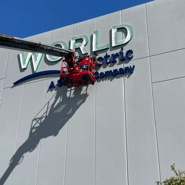 Workers install a large World Atlantic Aerospace sign on a building using a lift.