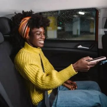 Smiling woman in yellow sweater paying with phone inside car.