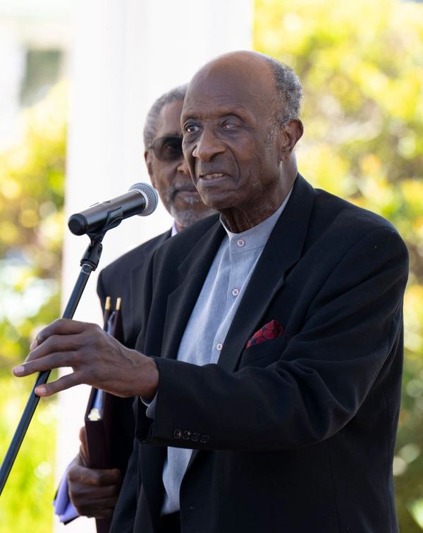 Elderly man speaking at a microphone outdoors.