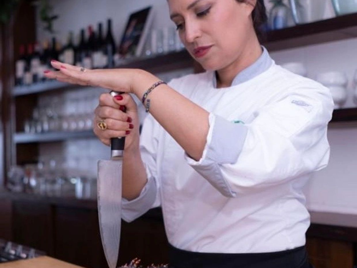 Femme chef affûtant un couteau à l'aide de sa main.