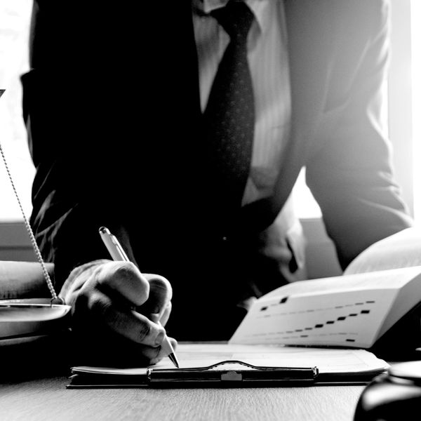A businessman in a suit writing on a clipboard with documents and a scale nearby.