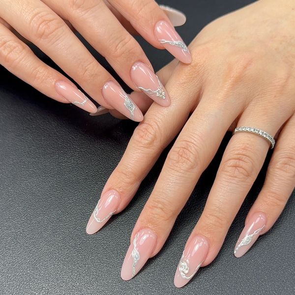 Elegant almond-shaped nails with nude polish and delicate silver designs.
