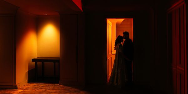 silhouetted Couple posing in a doorway, illuminated by a soft light in a dimly lit room.Pre wedding