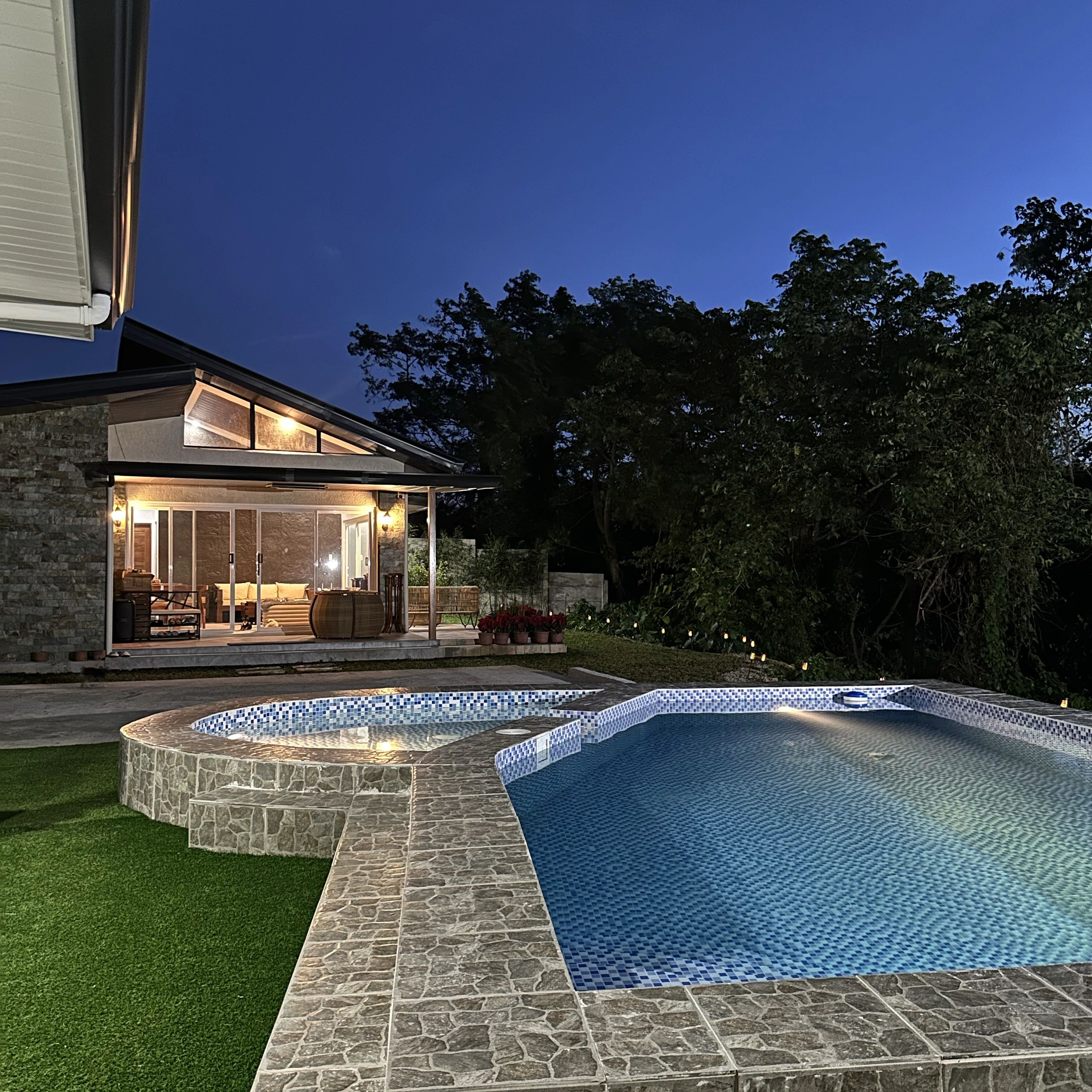 Modern house with illuminated pool and hot tub at dusk.