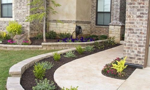 several tees and bushes planted in walkway at front of house
