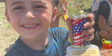 Young boy happily holding a fishing trophy outdoors.