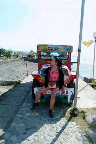 Woman sitting on a colorful jeepney near the waterfront.