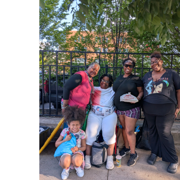 Five people, including a child, posing happily outdoors on a sunny day.