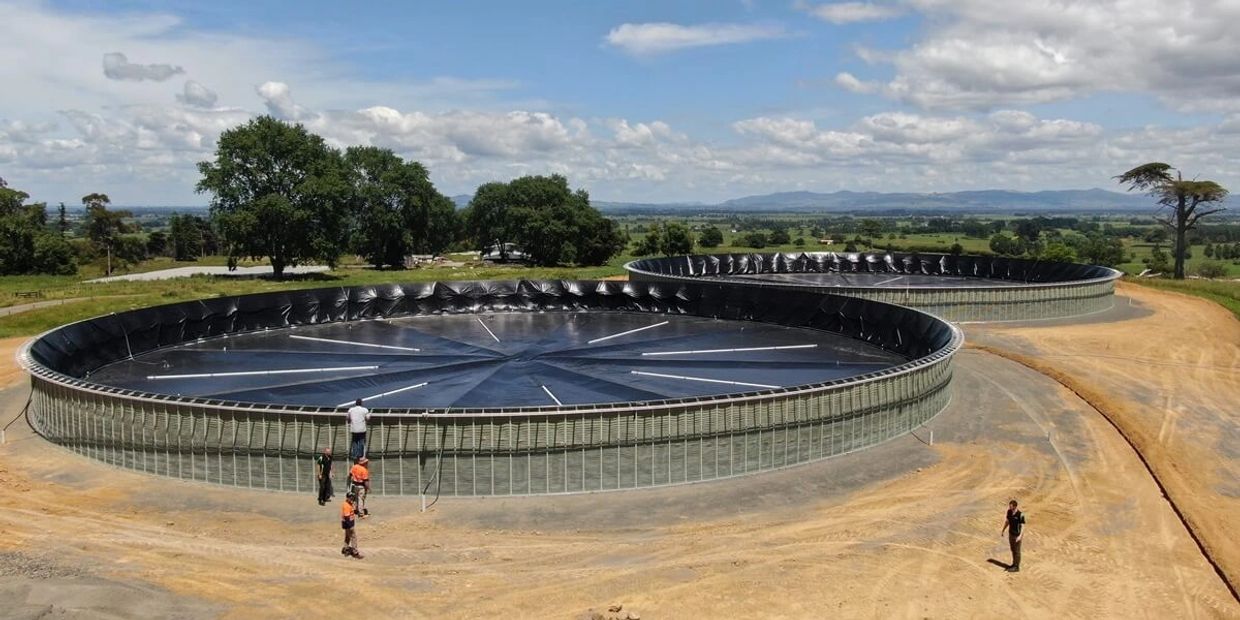 Two large circular water tanks with people around them in a rural setting.