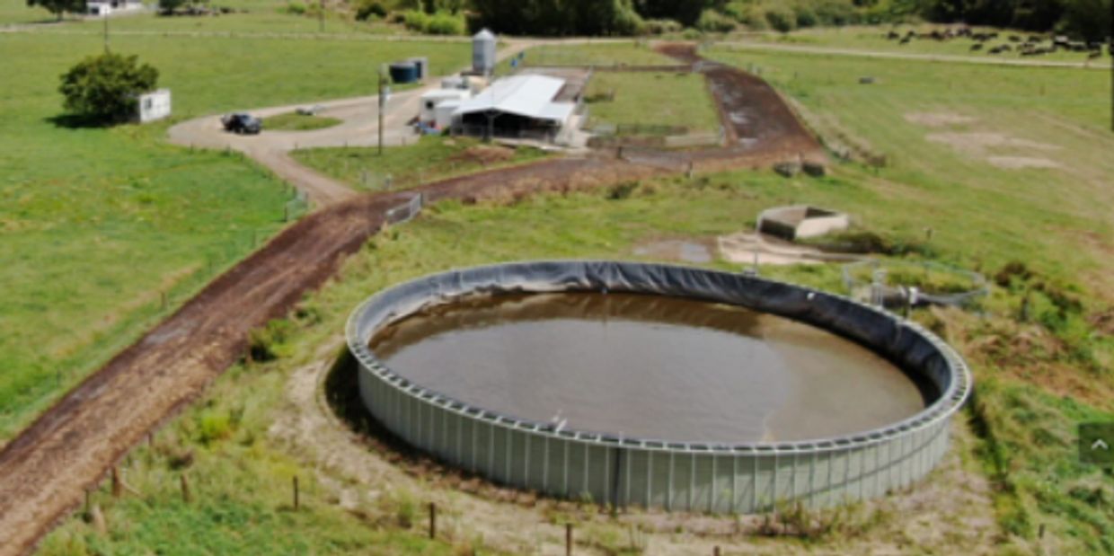 A large circular water tank on a farm with green fields and buildings in the background.