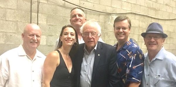 Group of six adults posing against a brick wall, including one man in a suit.