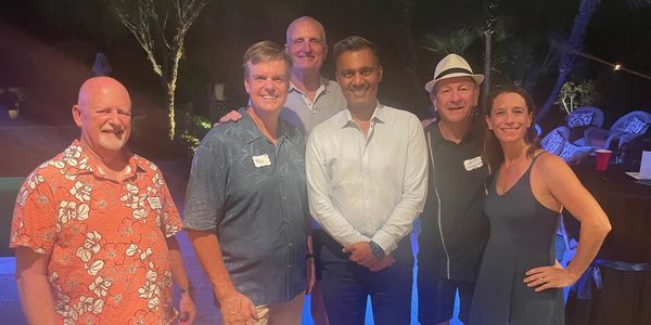 Group of six adults smiling at an outdoor evening gathering.