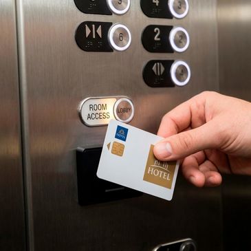 Hand holding hotel key card to activate elevator room access button.