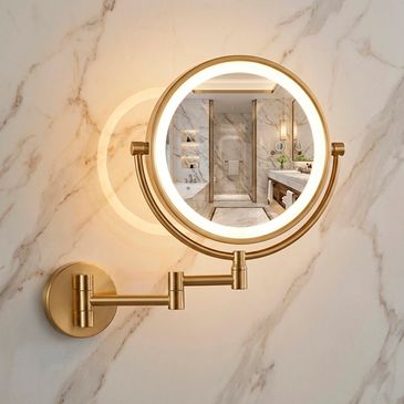 Brass wall-mounted magnifying mirror with built-in lighting in marble bathroom.