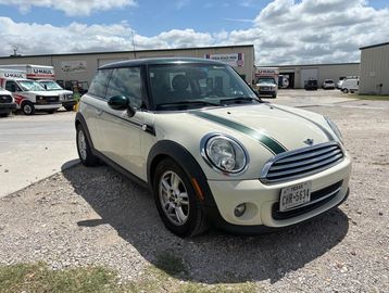 White Mini Cooper with green racing stripes parked on gravel.