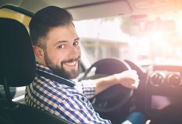 A smiling man driving a car, looking back.