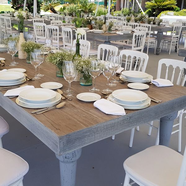 mesas de madera con sillas blancas montadas con vajillas, centros de mesa y copas para evento 