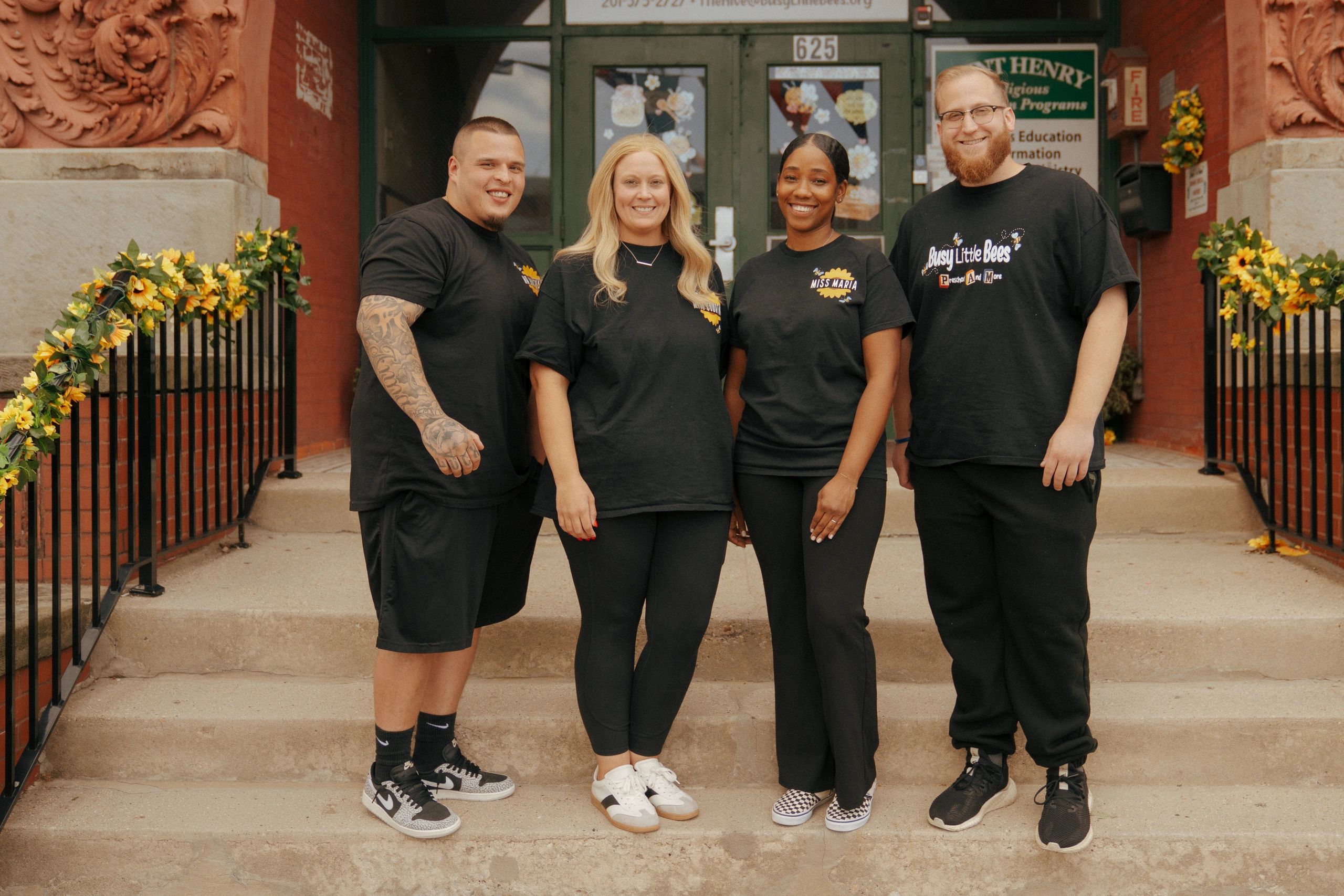 Four smiling colleagues standing on outside steps decorated with sunflowers.