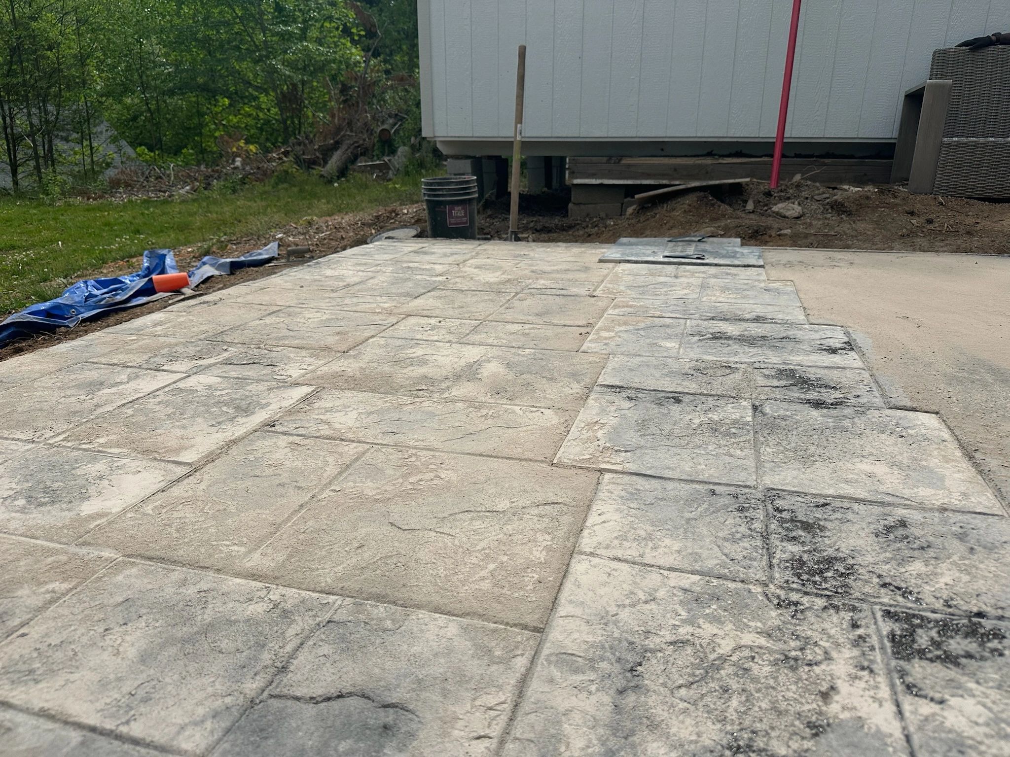 Partially completed stone patio with tools nearby in a backyard.