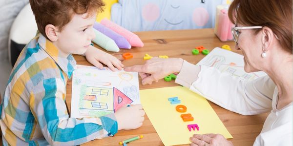 a little boy with his house drawing showing it to his teacher