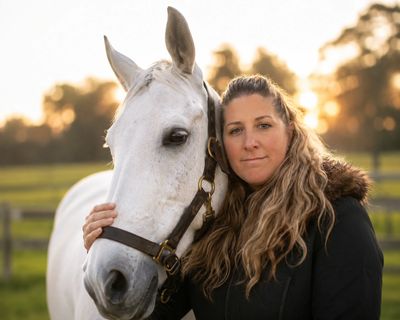 Woman embracing a white horse outdoors at sunset.