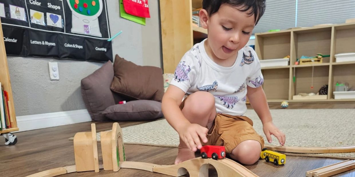 A young boy plays with a wooden train set on the floor.